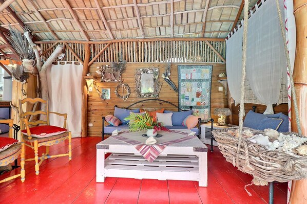 A cozy room with a wooden ceiling, a sofa with cushions, a coffee table with a decorative centerpiece, and a wicker basket.