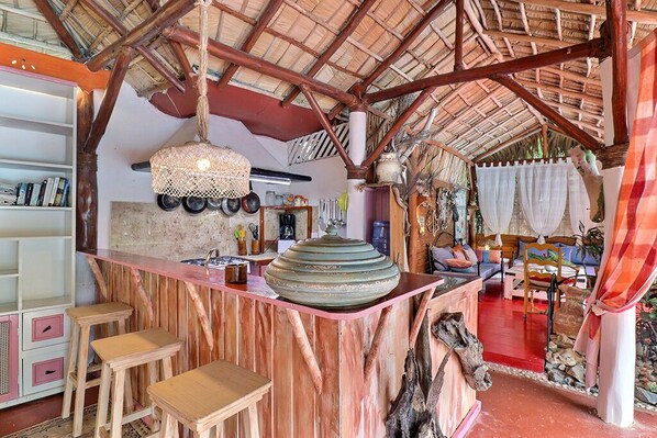 A rustic kitchen with a central island, wooden stools, and a hanging light fixture.