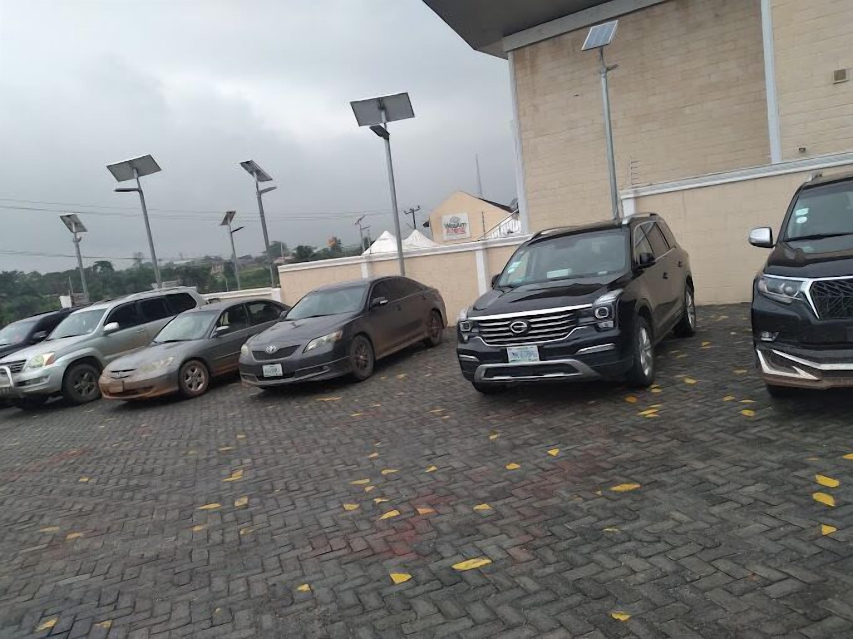 Un estacionamiento con varios autos, incluyendo un SUV negro y un sedán plateado, y un edificio con fachada color beige al fondo.