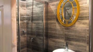 A bathroom with a glass-enclosed shower, a round mirror with a gold frame, and a white sink.