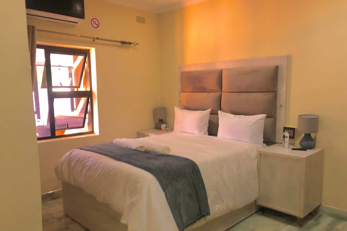 Habitación de hotel con una cama grande, dos mesitas de noche con lámparas, una ventana con vistas y un aire acondicionado instalado en la pared.