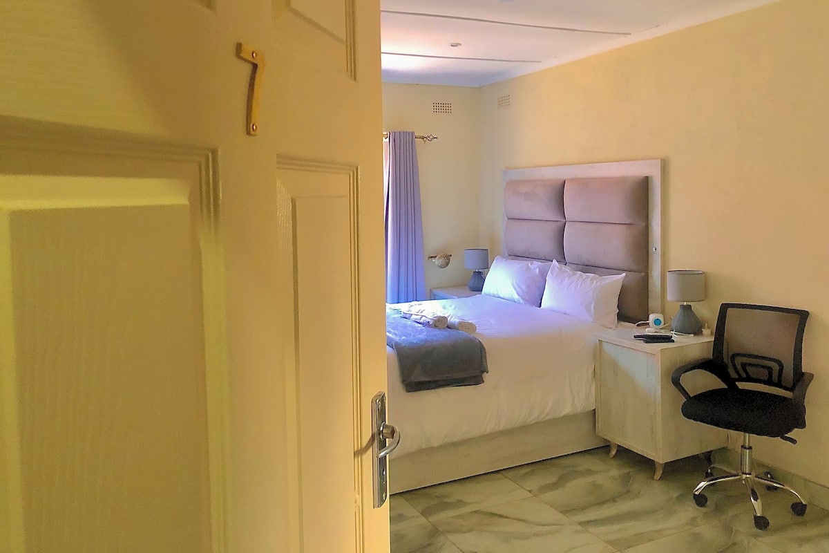 Una habitación de hotel con una cama, mesita de noche, silla y cortina.