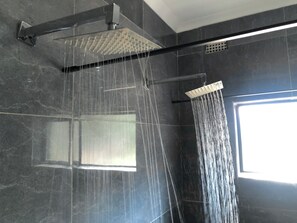 A modern shower with multiple heads, a control panel, and a window providing natural light. - Casa Favorita (Harare)