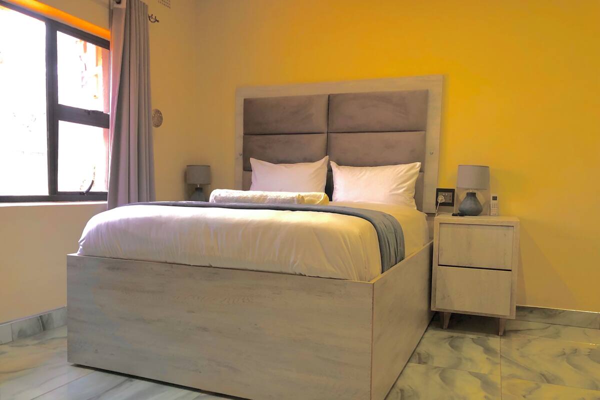 Un dormitorio con una cama grande, una mesita de noche con lámpara y una ventana con cortinas.