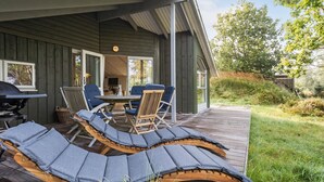 Een overdekt buitengebied met een tafel, stoelen, een barbecue en loungestoelen met kussens.