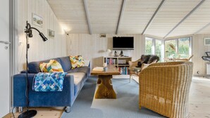 Een gezellige woonkamer met een blauwe bank, een rieten fauteuil, een houten salontafel en een televisie aan de muur.
