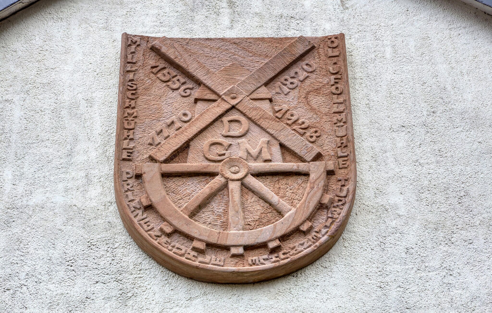 A stone emblem with a compass, crossed swords, and dates 1556, 1770, 1820, 1928, and 1945.