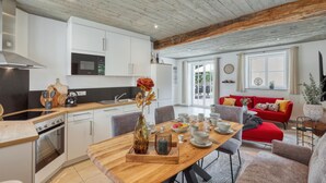 Eine moderne Küche mit weißen Schränken, einem Holztisch im Essbereich und einem roten Sofa im Wohnzimmer.