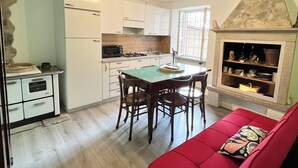 A compact kitchen with white cabinets, a dining table with chairs, a red sofa, and a stone fireplace. - SMILE          (Berzo)