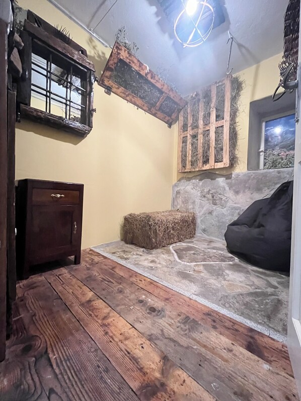 A rustic room with a stone wall, wooden floor, a wooden cabinet, a hay bale, and a black bean bag.