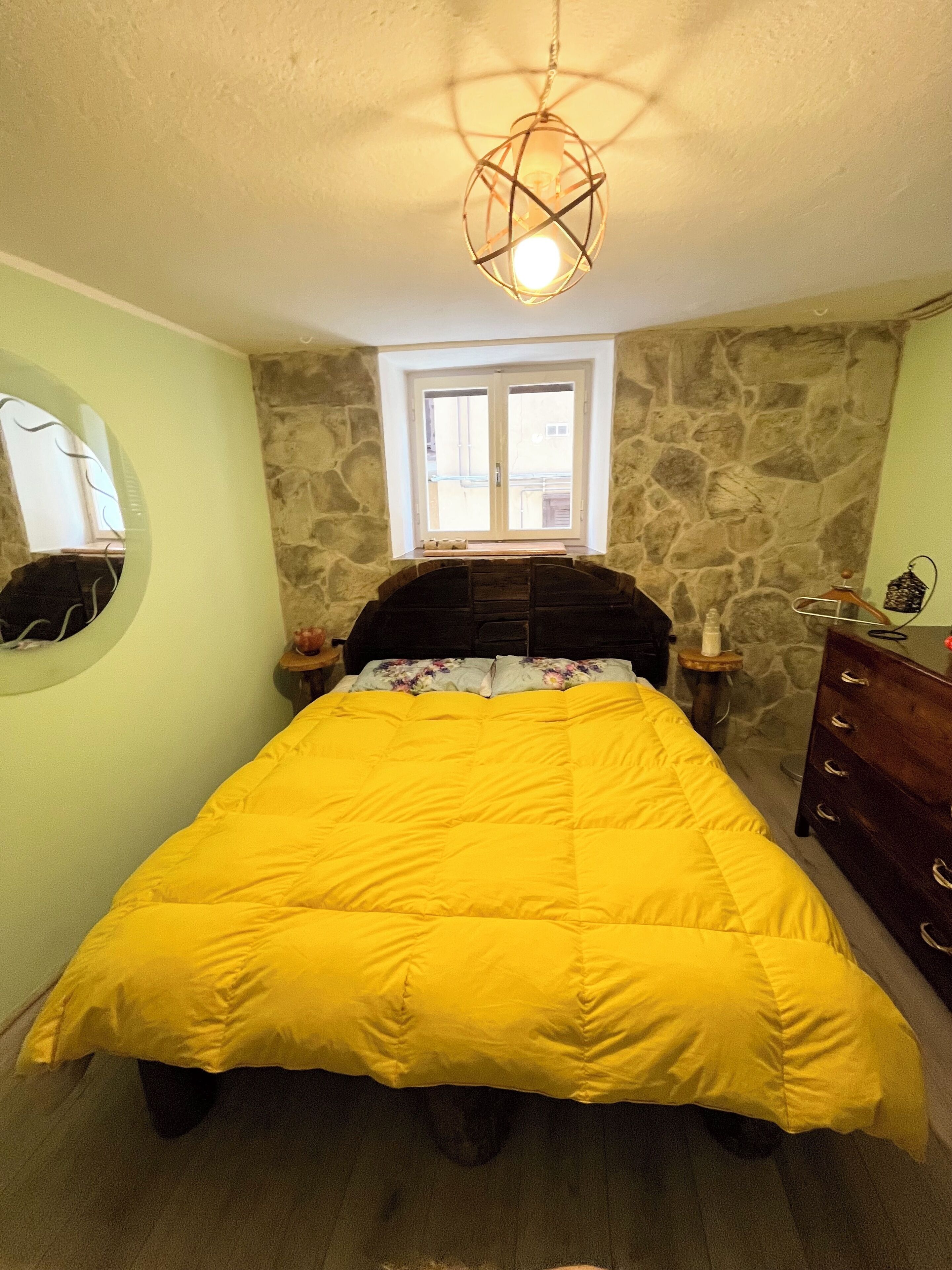 A bedroom with a bed, a dresser, a mirror, a window, and a unique light fixture.