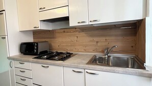 A modern kitchen with white cabinets, a gas stove, a microwave, and a sink. - SMILE          (Berzo)