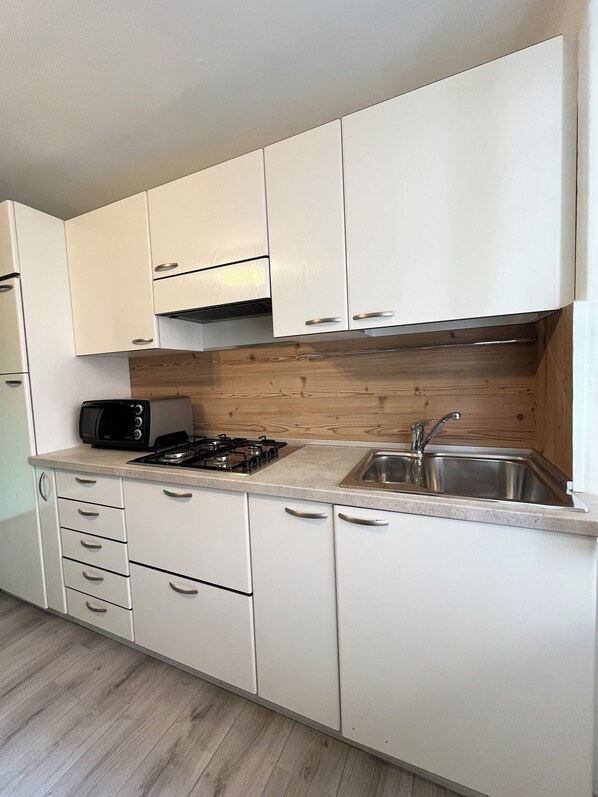 A modern kitchen with white cabinets, a gas stove, a microwave, and a sink.