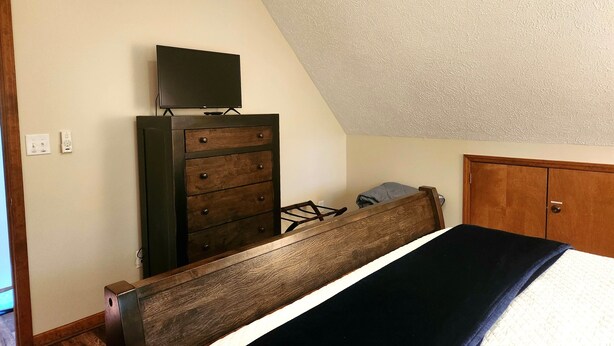 Un dormitorio con cama, cómoda, televisor encima y una puerta.