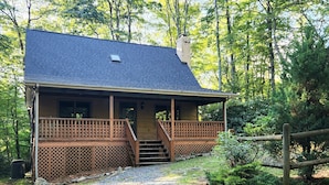 Eine Hütte mit Veranda, Holzbalkonen und einem Schotterweg, umgeben von Bäumen.