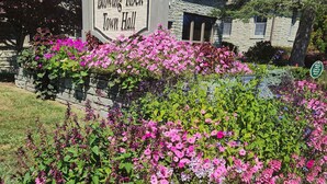 Schild für das Blowing Rock Rathaus mit einem Steinhaus im Hintergrund und einem Blumenbeet im Vordergrund.
