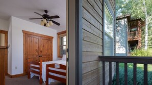 Ein Zimmer mit Holztür, Deckenventilator, Tisch mit Stühlen und Blick auf eine Holzterrasse und Grünfläche.