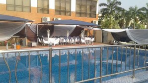 Une piscine avec une rambarde en métal, des tables avec des chaises blanches et des parasols.