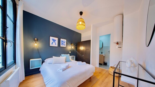 Une chambre à coucher moderne avec un grand lit, des tables de chevet, un luminaire suspendu et une vue sur la salle de bain.