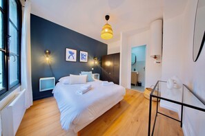 Ein modernes Schlafzimmer mit einem großen Bett, Nachttischen, einer Pendelleuchte und Blick ins Badezimmer.