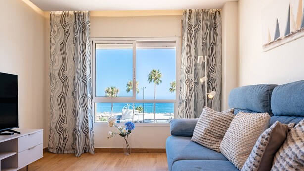 Ein modernes Wohnzimmer mit einer Couch, einem Fernseher und Meerblick durch große Fenster.