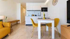 Un salon moderne avec un canapé, une table à manger et des chaises, une cuisine en arrière-plan et une horloge murale.