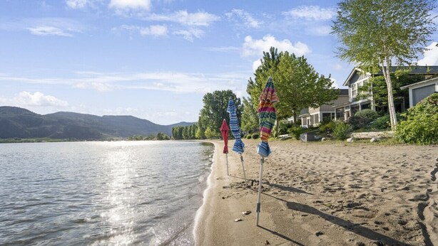 En strand med fri sikt över vattnet, en sandstrand och en rad färgglada parasoller.