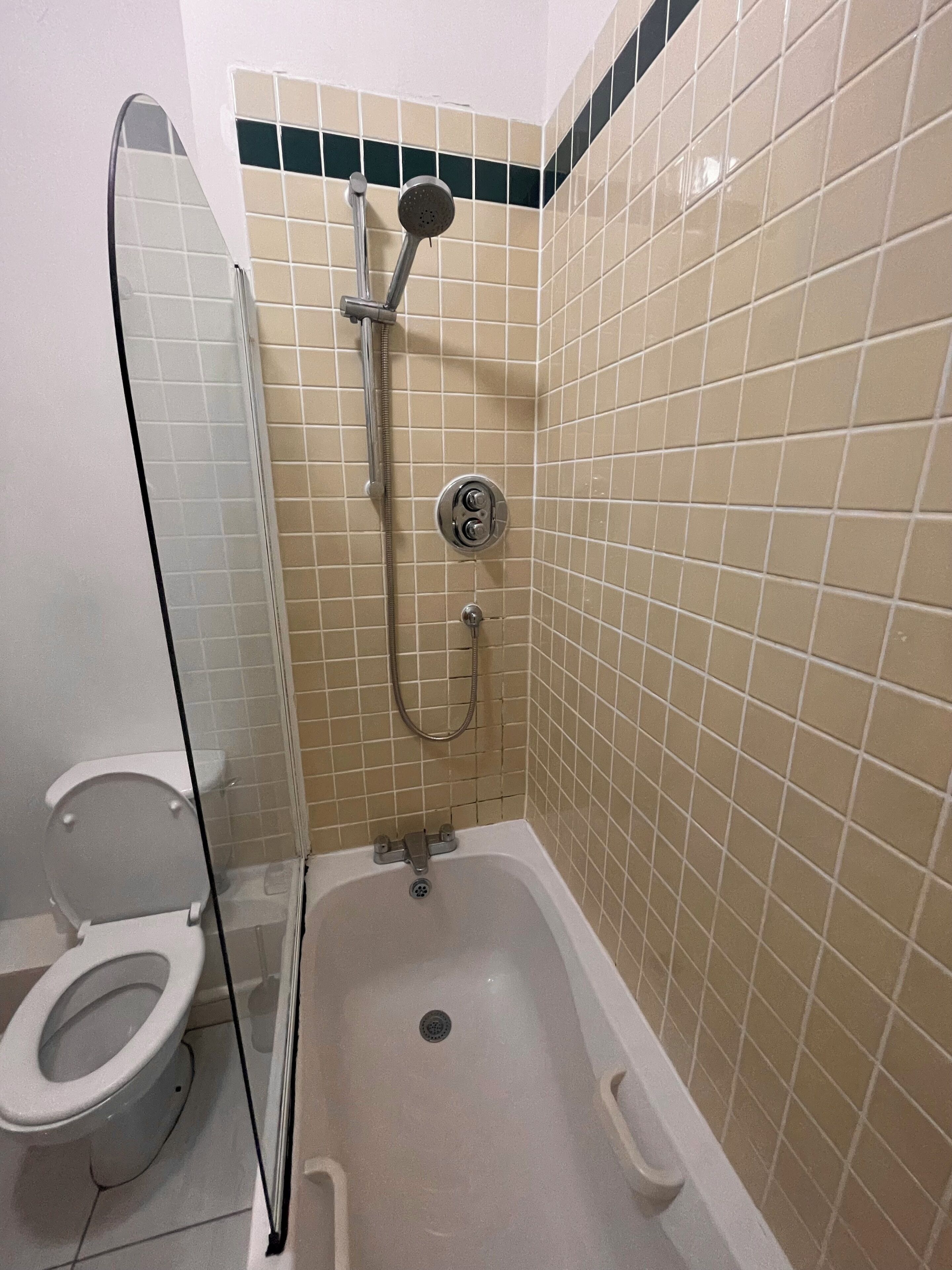 A small bathroom with a toilet, a shower with a glass door, and tiled walls.