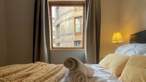 Ein ordentlich bezogenes Bett mit gerolltem Handtuch, einer strukturierten Decke und einer Lampe auf dem Nachttisch.