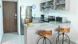 A modern kitchen with a stainless steel refrigerator, a clock, and a bar area with stools. - Modern & Spacious APT - Wifi, Gym, Pool, A/C (San Salvador)