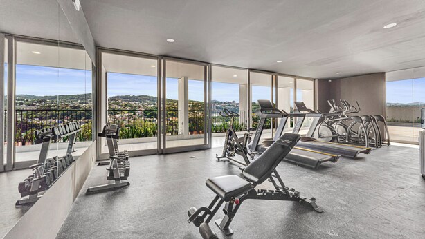 A modern gym with various exercise equipment, large windows offering a city view. - Modern & Spacious APT - Wifi, Gym, Pool, A/C (San Salvador)