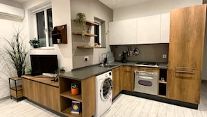 A modern kitchen with wooden cabinets, a built-in washing machine, and a large window.