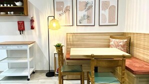 A cozy room with a wooden bench, a small table, and a floor lamp. There are framed pictures on the wall and a shelf with decorative items.
