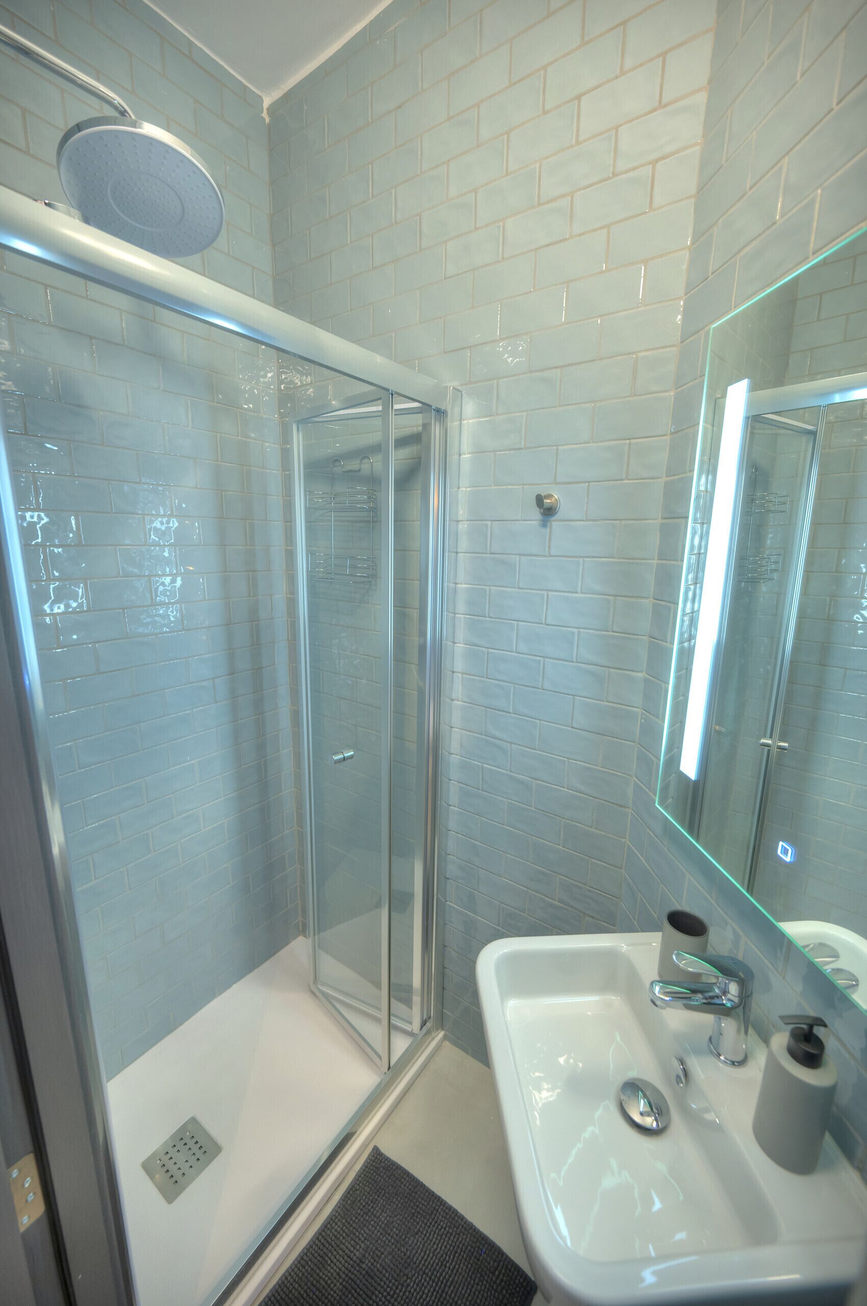 A bathroom with a glass-enclosed shower, a white sink with a mirror, and light blue tiled walls.
