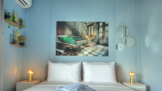 A hotel room with a bed, two bedside tables, a painting of a vintage car, and a wall-mounted mirror. - Stylish, large 3bedroom, seafront terrace GOSLM-13 (Sliema)