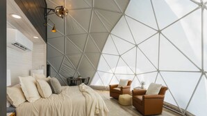 Een moderne slaapkamer met een geometrisch plafond, een groot bed, twee banken en een tafeltje met een plant.