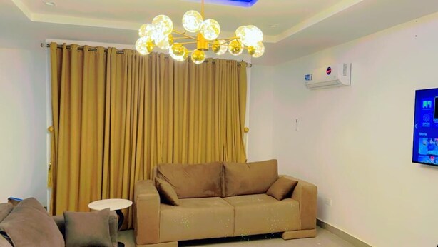 A living room with a brown sofa, a small round table, and a modern chandelier.