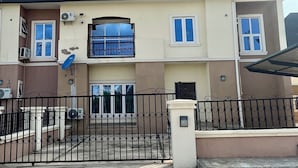 A two-story residential building with a satellite dish, air conditioning units, and a gated entrance.