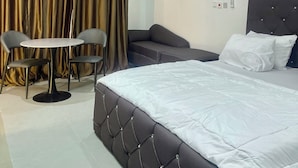 A modern hotel room with a large bed, a small round table with two chairs, a sofa, and a curtain.