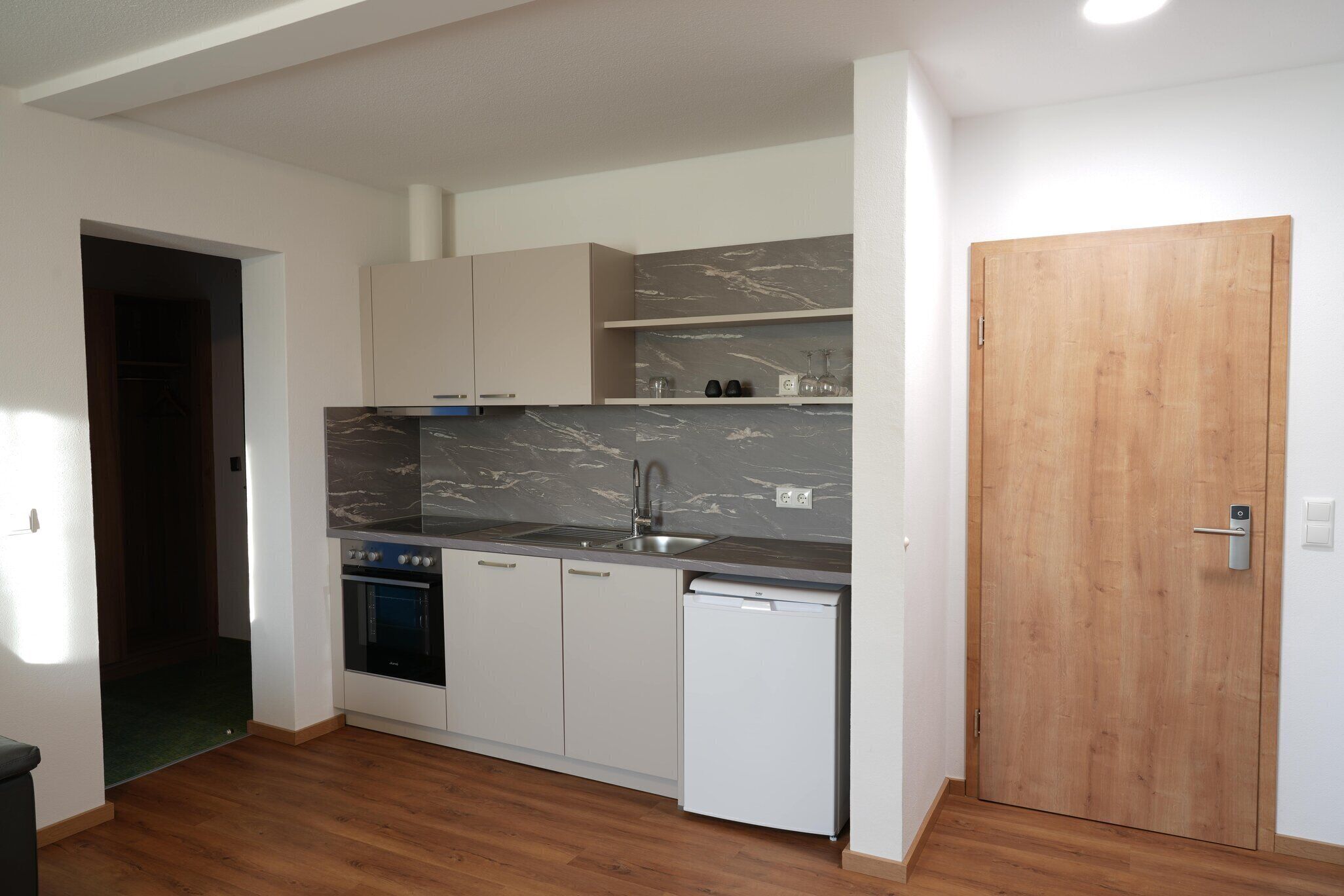 Een compacte keuken met een ingebouwde oven, een vaatwasser en een marmeren spatwand.