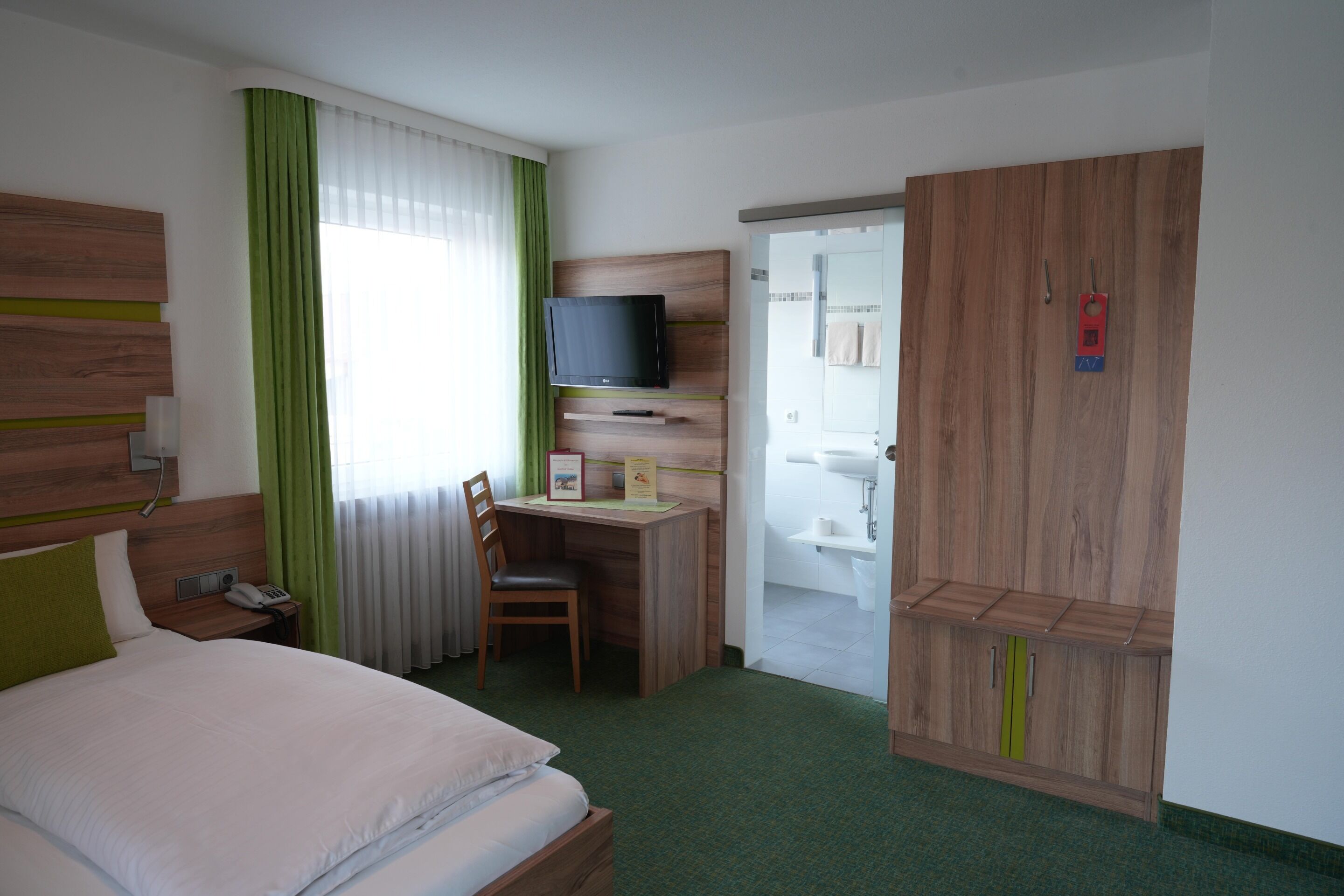 Ein Hotelzimmer mit Bett, Schreibtisch mit Stuhl, Fernseher, Kleiderschrank und Badezimmer.