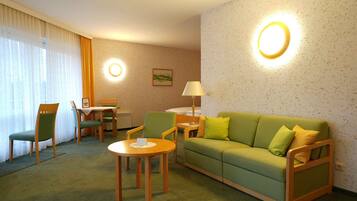 A hotel room with a green sofa, two chairs, a small table, a lamp, and a painting on the wall.