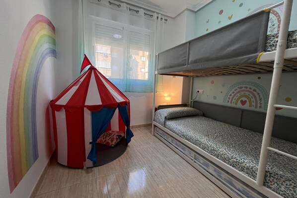 Une salle de jeux pour enfants avec des lits superposés, une tente et une fresque murale aux couleurs de l’arc-en-ciel.