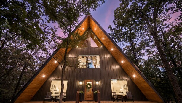 A wooden cabin with a triangular roof, large windows, and a porch with seating.