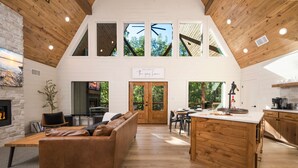 A spacious loft-style living area with a wooden ceiling, a fireplace, a large brown leather sofa, and a kitchen with wooden cabinetry and a central island.