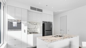A modern kitchen with white cabinetry, a built-in oven, a black refrigerator, and a marble countertop. - Swainson on Hindmarsh (Adelaide)