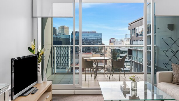 A modern living room with a large glass sliding door leading to a balcony, a flat-screen TV, a glass coffee table, and a sofa. - Swainson on Hindmarsh (Adelaide)