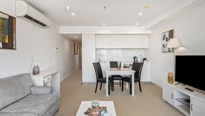 Uma sala de estar moderna com um sofá cinzento, uma mesa de centro com objetos decorativos, uma televisão e uma área de jantar com mesa e cadeiras.