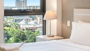 Quarto de hotel com uma grande janela que oferece vista para o horizonte urbano e um edifício com telhado em cúpula.