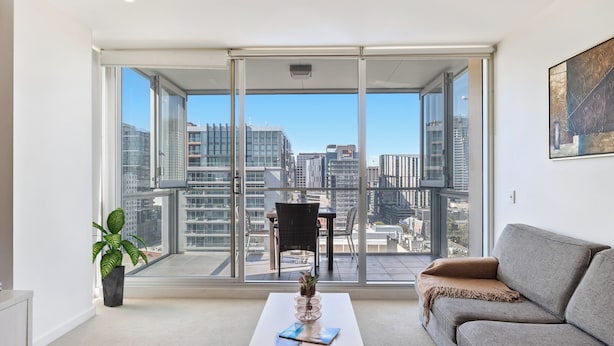 Uma sala de estar moderna com uma grande porta de vidro deslizante que dá para uma varanda com vista para a cidade.